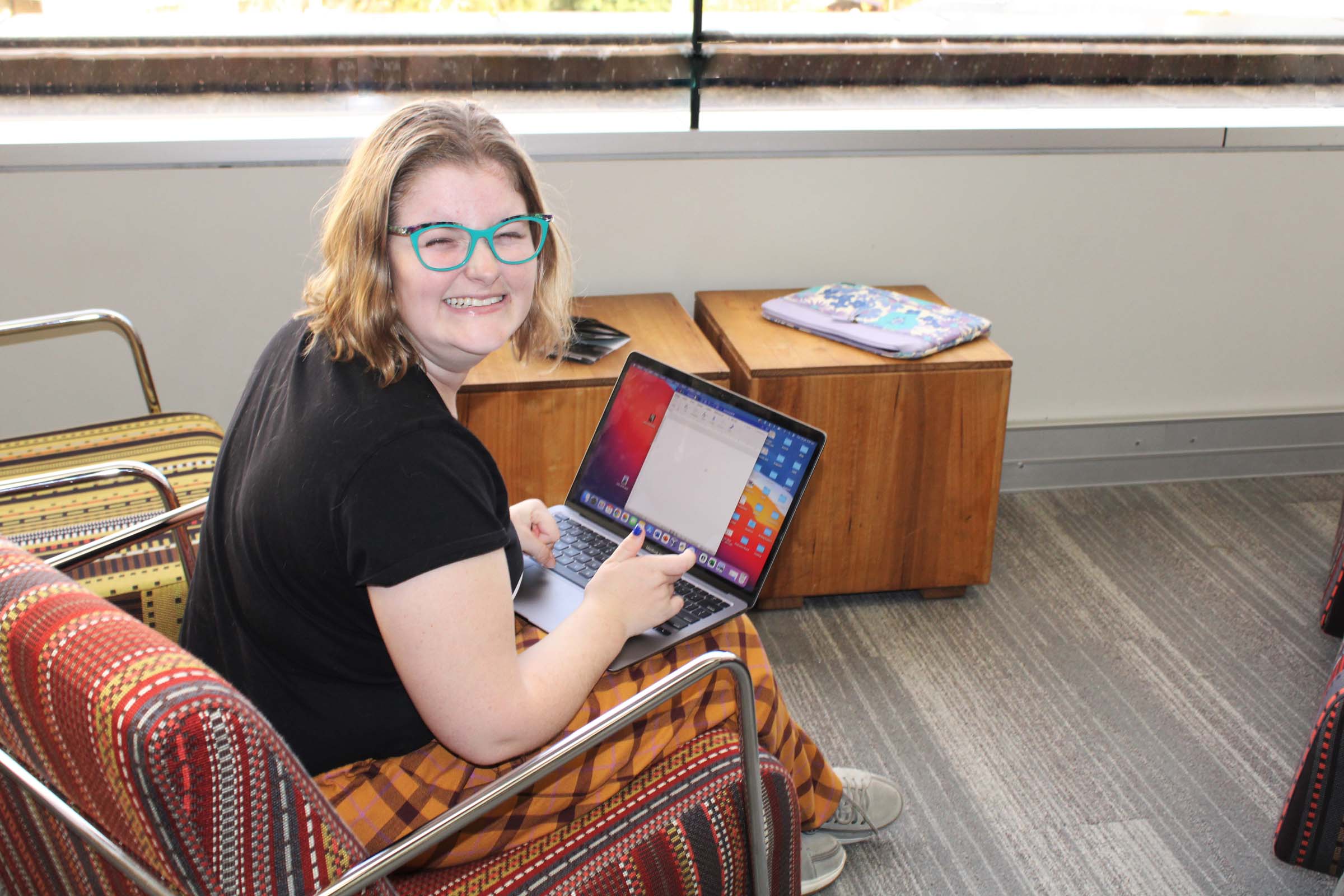 A woman sits at her computer at a library with a laptop on her lap. A woman sits at her computer at a library with a laptop on her lap.