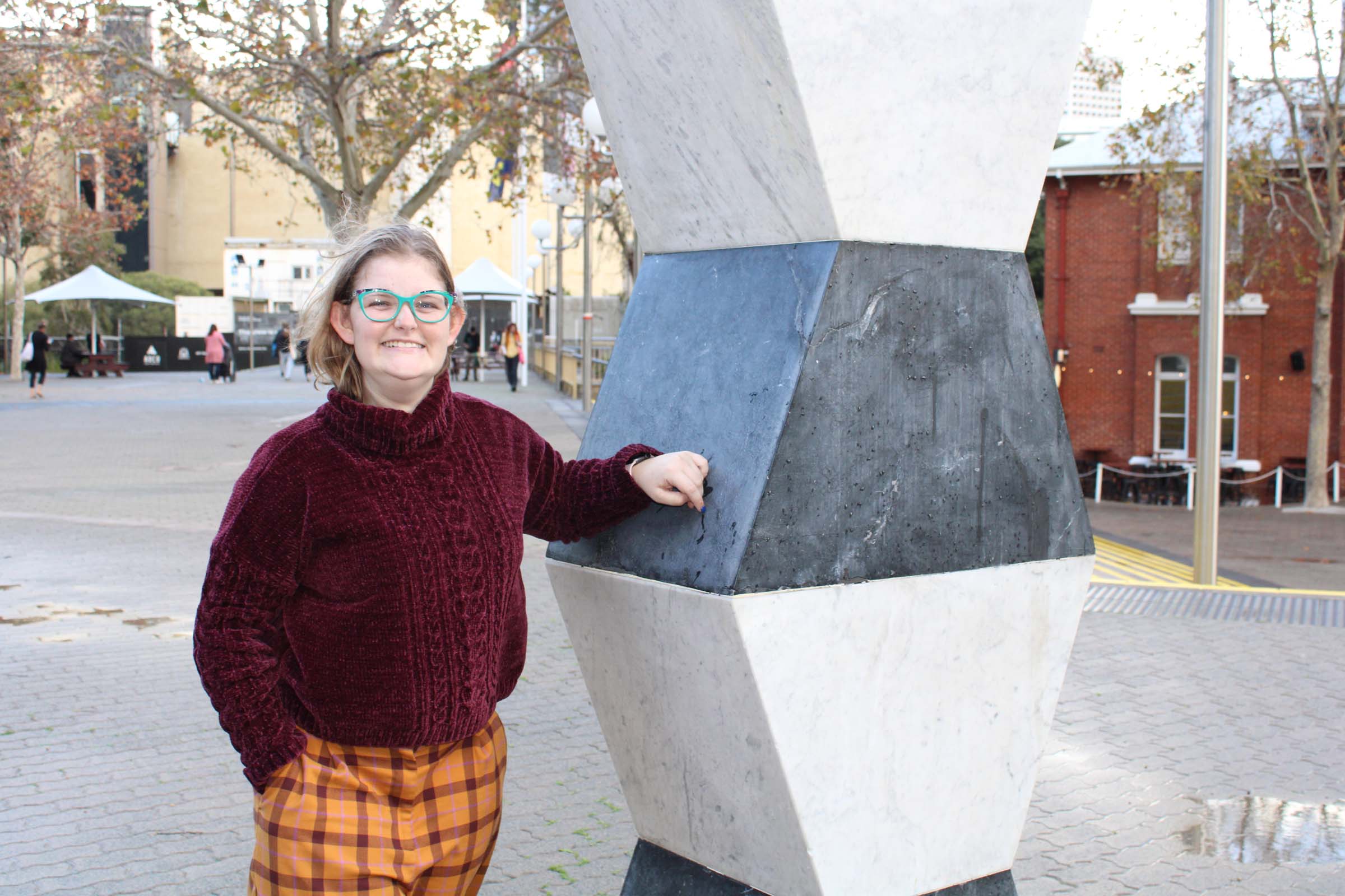 A lady smiles as she rests her arm on a sculpture in a busy city mall. A lady smiles as she rests her arm on a sculpture in a busy city mall.
