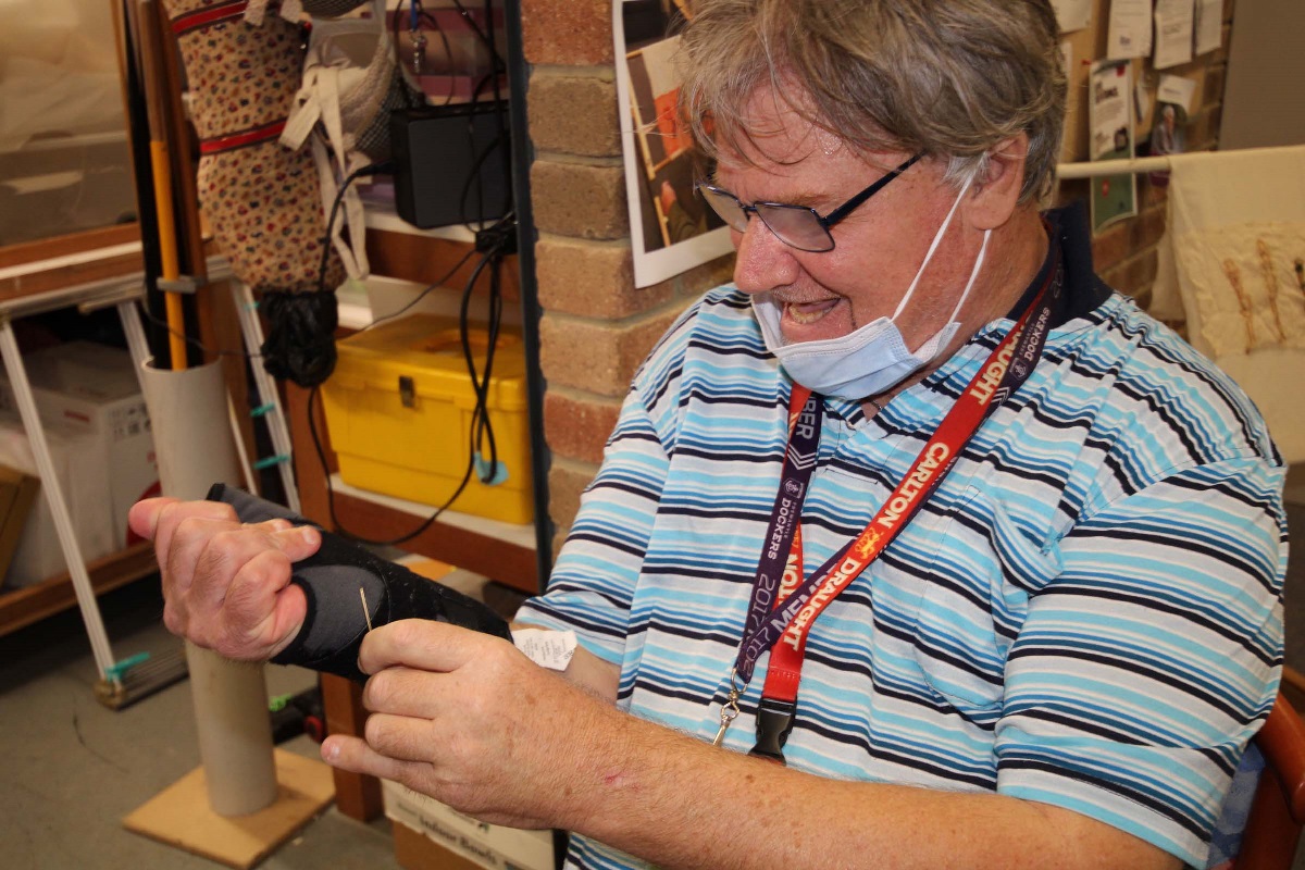 A man hooks a needle into his arm brace while he works and smiles.