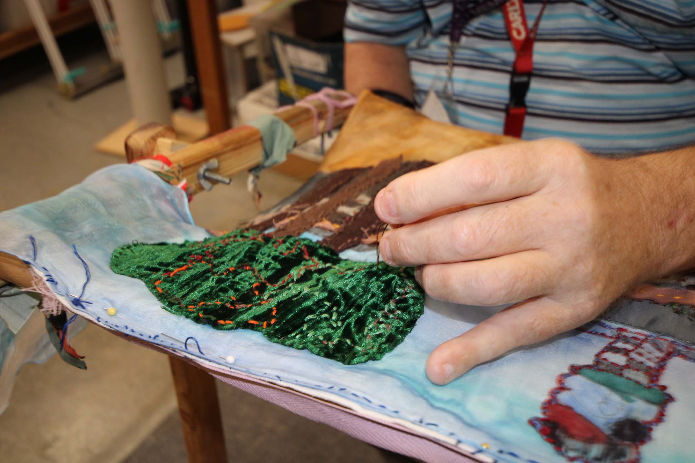 A close-up shot of a man using a needle on an adaptive frame to do embroidery. A close-up shot of a man using a needle on an adaptive frame to do embroidery.