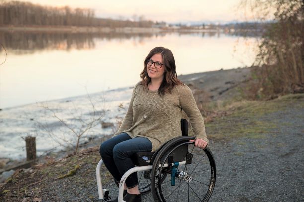 A lady in wheelchair is smiling with the lake behind her. A lady in wheelchair is smiling with the lake behind her.
