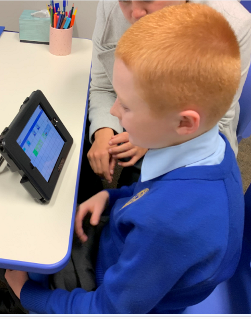 A little boy uses an AAC device with the help of a woman.