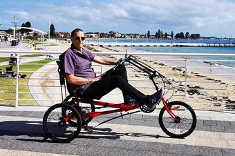 A man is seated on his recumbent trike by the seaside