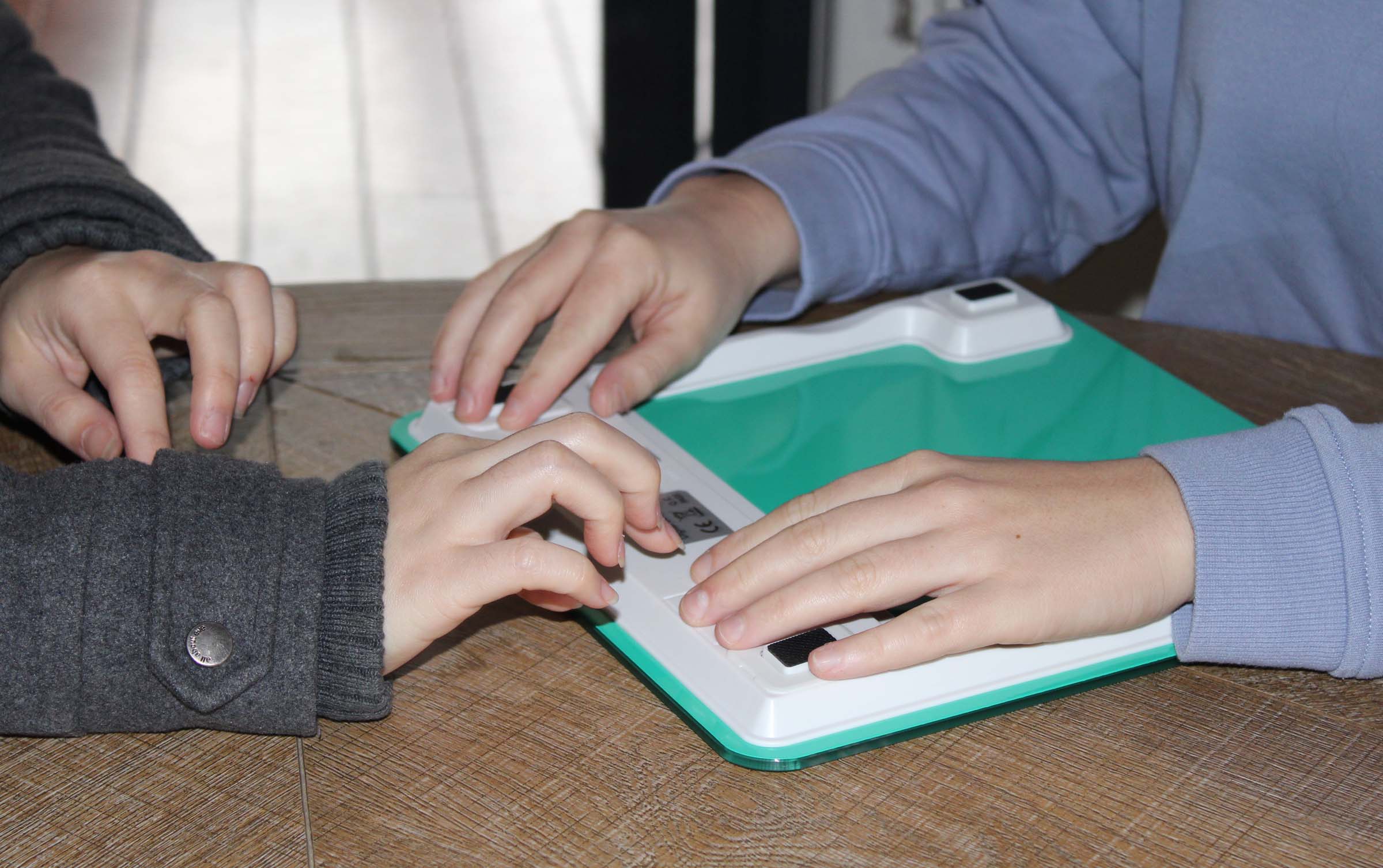 Two women place their hands on top of an electronic scale on a wood surface table.