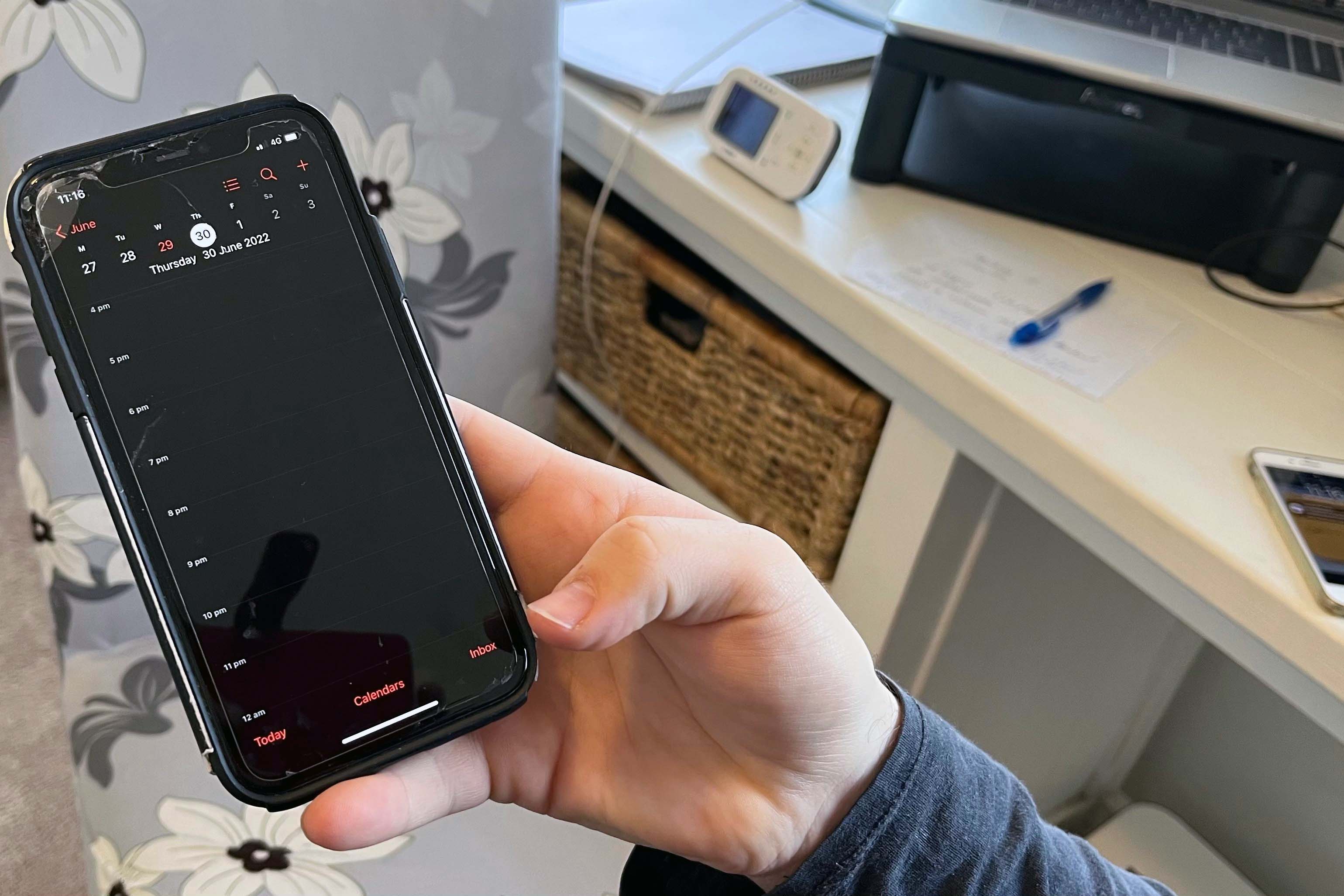 A man is holding a mobile phone with a calendar app showing on the screen.