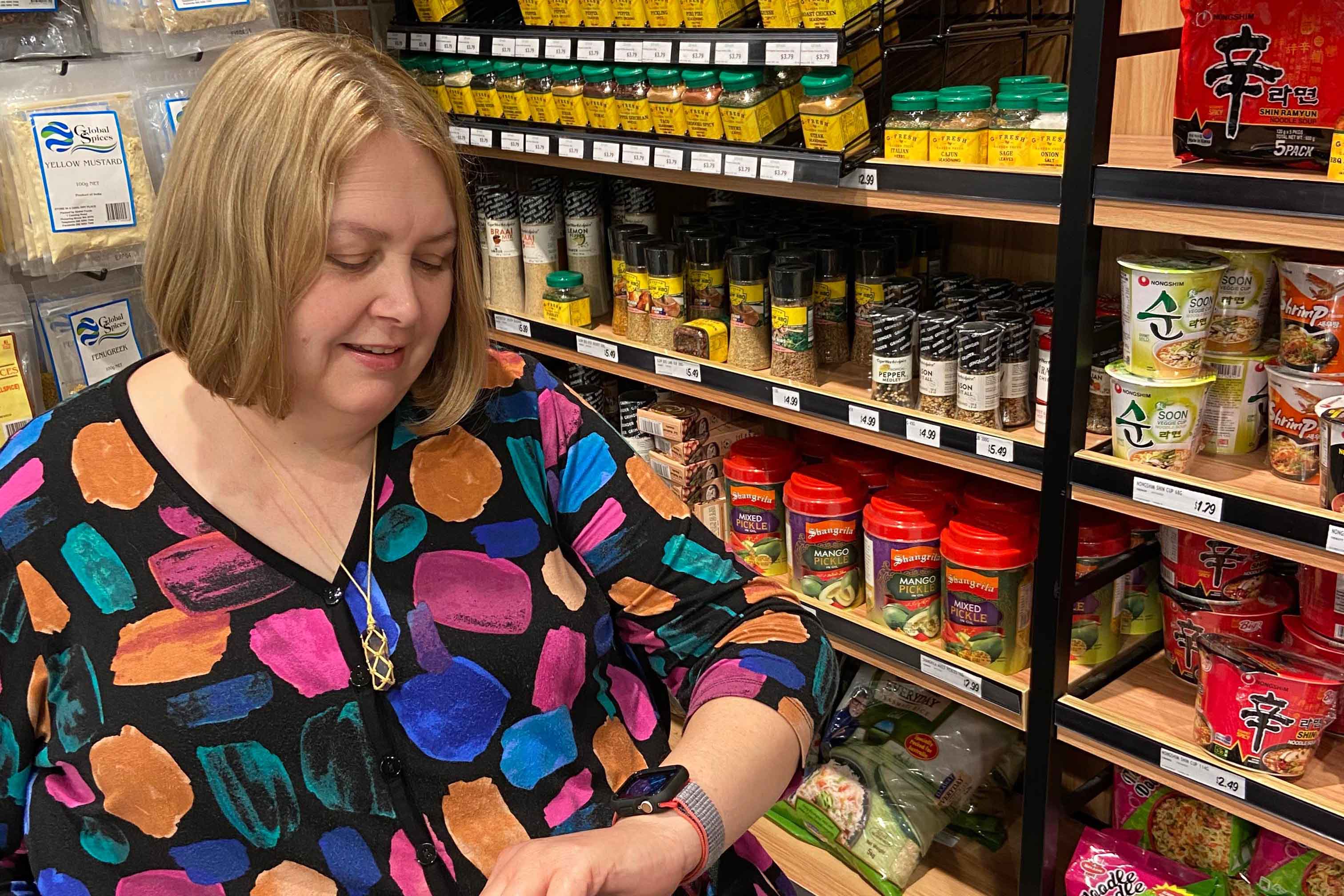 A young lady stands smiling as she brings her smart watch up to towards her face to read it. A speech bubble is in the background with the words, Why self-advocacy is important for assistive technology (AT) users.