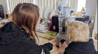 A woman and her young son are leaning on a kitchen bench facing away from camera starting to use the Kitchen Wizz 8.