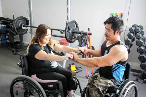 A lady and a man workout in the gym from their wheelchairs.