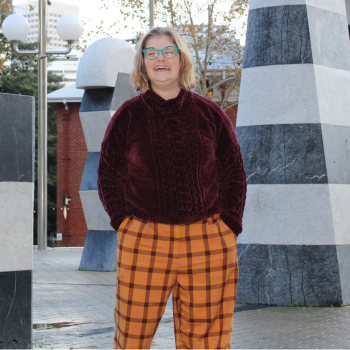 Photo of a young person standing outside, smiling with their hands in their pockets