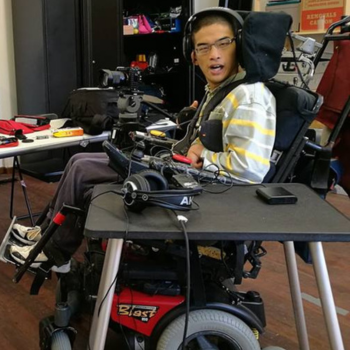 Photo of a young man in a powered wheelchair in a studio with headphones and microphones