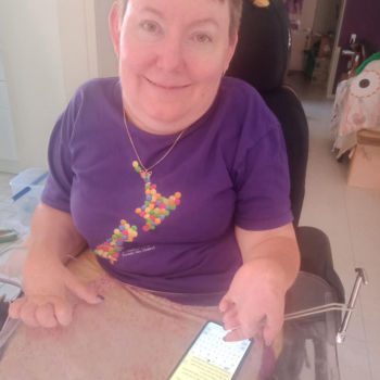 Photo of a woman typing a story on her mobile, which rests on a board on her lap