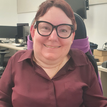 Photo of a woman in a maroon shirt wearing glasses and smiling