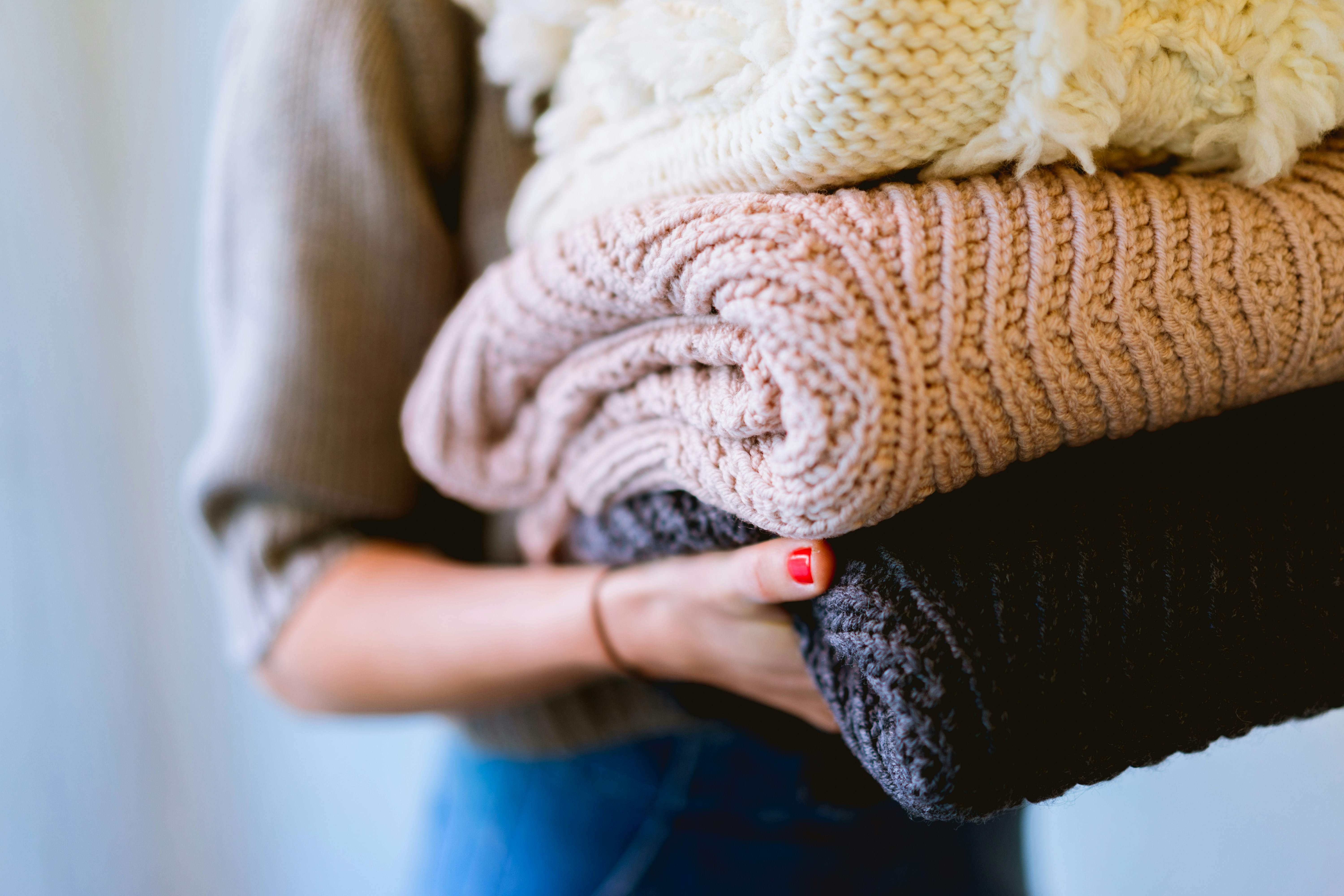 dan-gold-aJN-jjFLyCU-unsplash Woman holding a neatly folded pile of knitted items