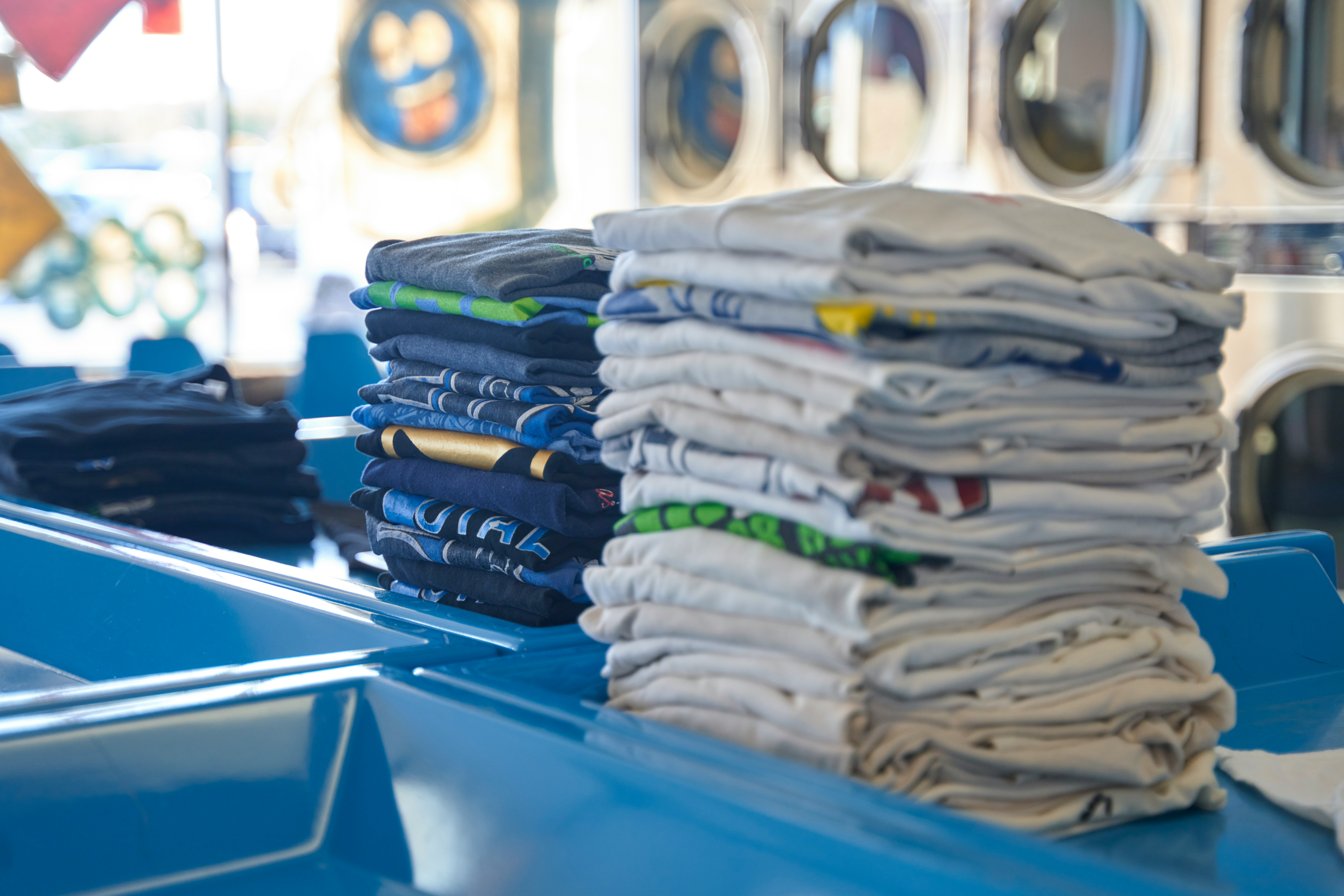 dan-lefebvre-APUvZYCjPJ0-unsplash Neatly folded stacks of clothes with a laundromat in the background