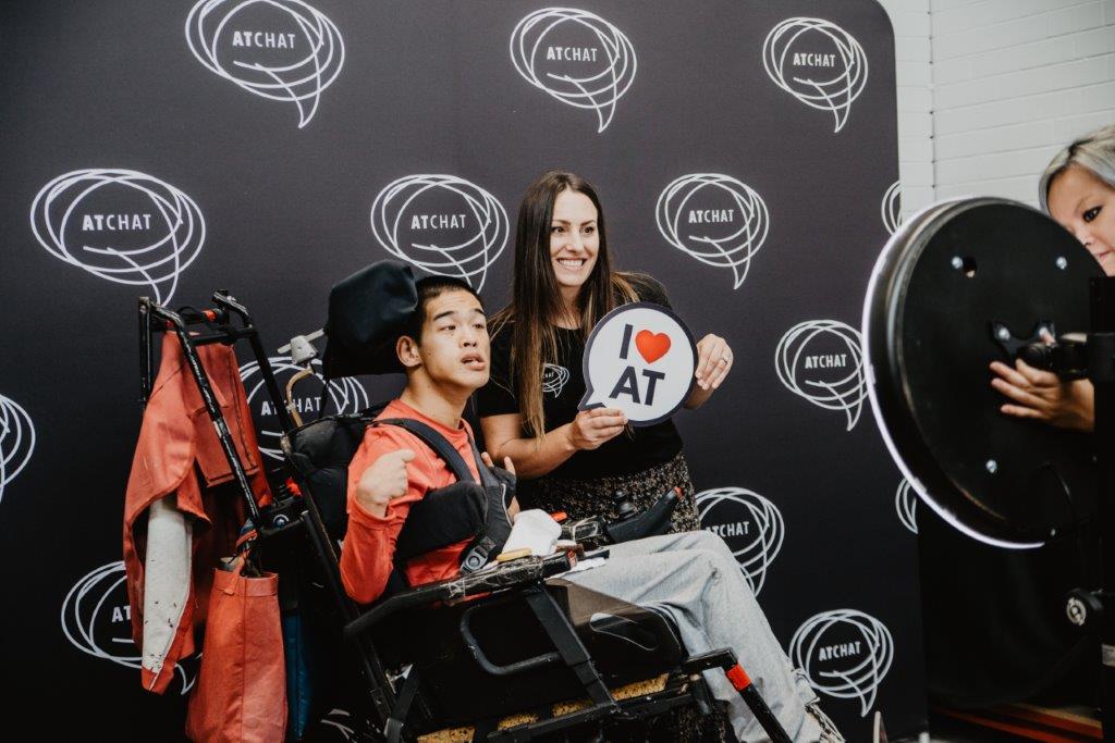 danielle_sam_photo man using power wheelchair with woman and speech bubble sign