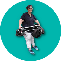 A lady stand smiling as she holds her folded rollator