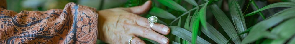 photo of a hand with a large pearl ring stroking green leaves