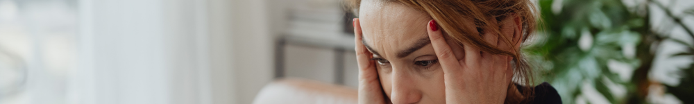 Photo of a woman holding her head, looking stressed while people stand around