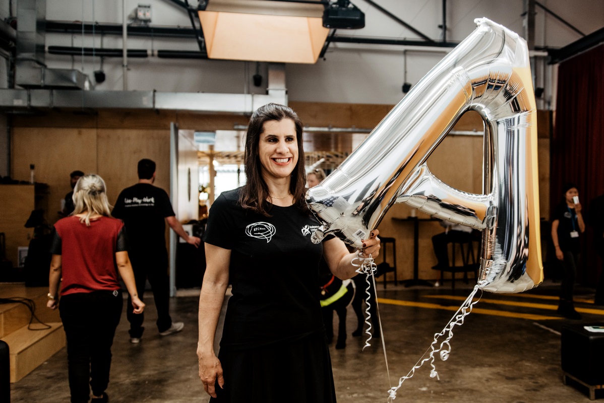 zel_resize woman in black at chat tshirt stands in front of at chat backdrop