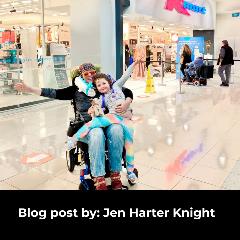 A lady is seated in a wheelchair with a young girl on her knee outside KMart. Both are smiling and the lady has her arms spread out wide. Several people including an older person using a mobility scooter are seen entering the store behind her.