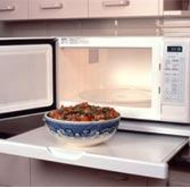 Microwave Open microwave has a shelf sticking out from underneath it. There is a bowl of food on the shelf.