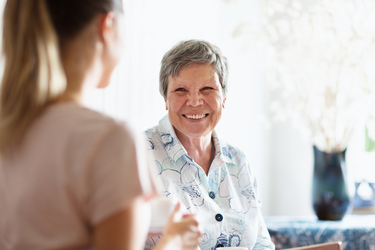A younger support worker supports an older woman in her home and they both smile.