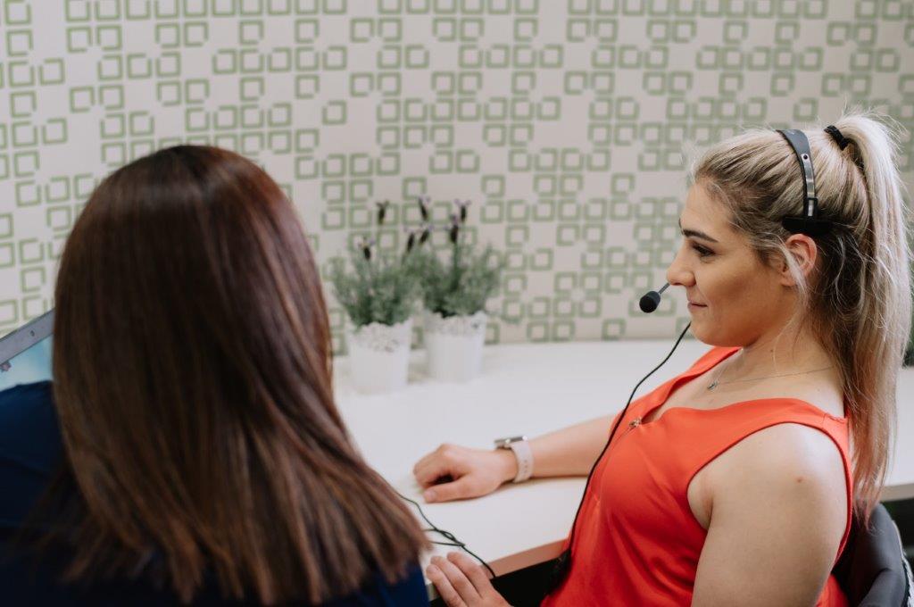 Customer focus_Home Office Back of female head brown hair sitting female with microphone headset sitting at desk