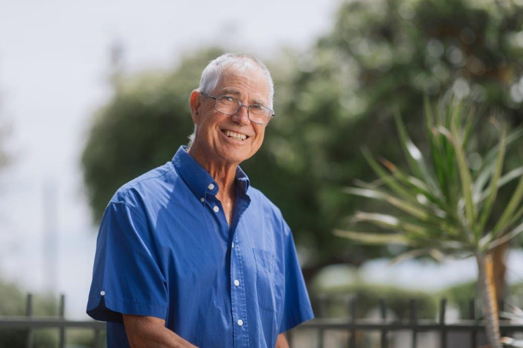 Male in blue shirt and glasses smiling while outside